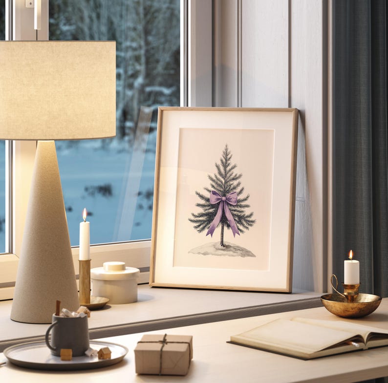 May include: A framed illustration of a small evergreen tree with a purple bow on a white background. The frame is on a wooden desk with a lamp, candles, and a book.