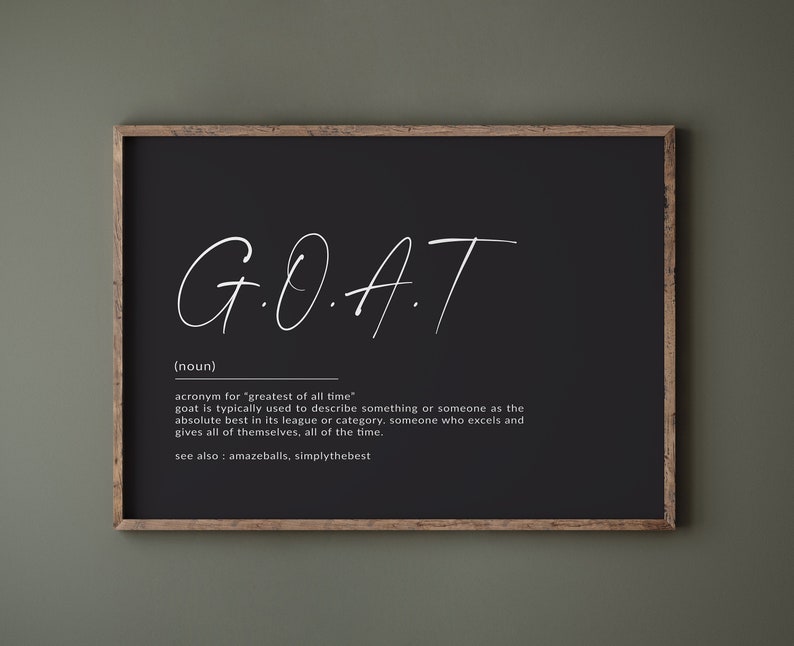May include: Black and white typography print with the acronym "G.O.A.T." defined as "greatest of all time". The print is framed in a dark wood frame.