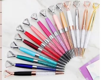 May include: A set of 12 diamond-shaped pens with glitter accents. The pens are in various colors, including pink, purple, red, blue, green, and gold. The pens have a clear barrel with glitter inside and a diamond-shaped top.