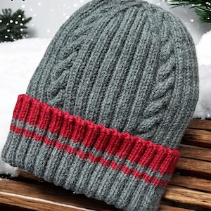 Peut inclure: Bonnet en tricot gris avec un bord rayé rouge et gris. Le bonnet est en tricot torsadé.