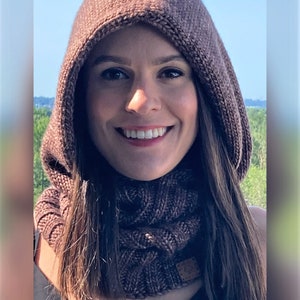 Könnte beinhalten: Ein brauner gestrickter Kapuzen-Schal mit einem Zopfmuster. Der Schal wird von einer Person mit langen braunen Haaren getragen.