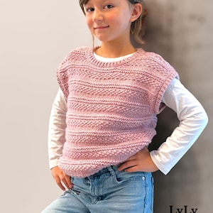 Peut inclure: Une jeune personne porte un gilet rose tricoté sur une chemise blanche à manches longues et un jean bleu. Le gilet présente un motif texturé. Le texte "LyLy Tricote Encore" est visible en bas à droite.