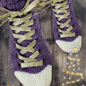 May include: Knitted purple slipper socks with white toes and gold ribbon laces. The socks have a gold star and the text "Lyly Tricote Encore". The socks are on a wooden surface.