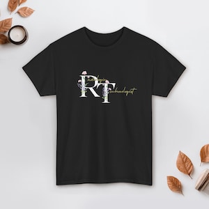 Puede incluir: Camiseta negra con la inscripción "Radiologic Technologist" en blanco y dorado. Las letras "RT" son grandes y están decoradas con flores rosas y moradas. Una camiseta informal para profesionales médicos.