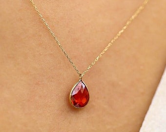 May include: A gold chain necklace with a red teardrop-shaped pendant.