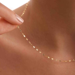 May include: A delicate gold chain necklace with a delicate, shimmering finish. The chain is made of small, flat links that are connected together to create a delicate and elegant look.