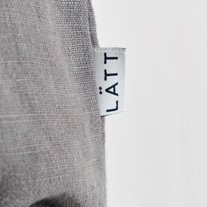 May include: Close-up of a gray fabric with a white tag. The tag has the word "L&Auml;TT" printed in black. The fabric appears to be linen or a similar woven material.