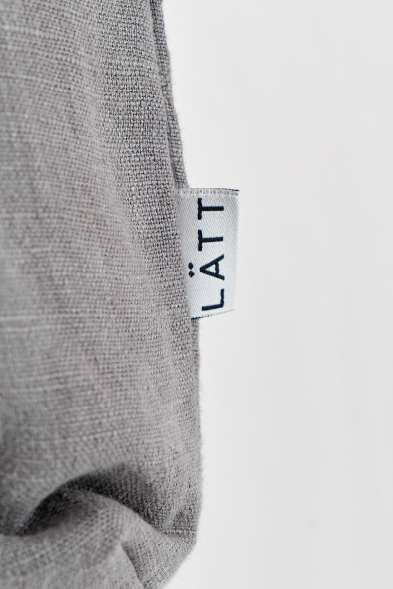 May include: Close-up of a gray fabric with a white tag. The tag has the word "L&Auml;TT" printed in black. The fabric appears to be linen or a similar woven material.