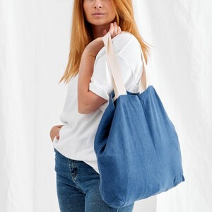 May include: A blue tote bag with cream-colored straps. The bag is made of a textured fabric and is carried over the shoulder. The bag is a simple, casual style.