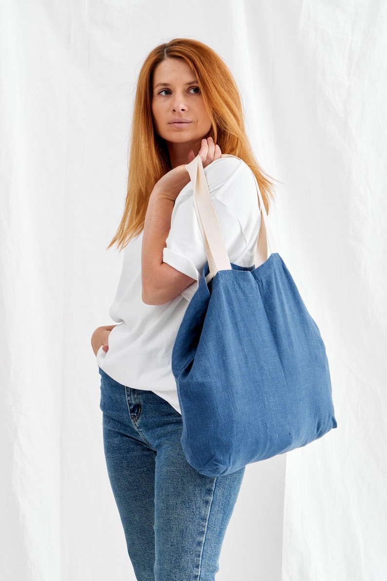 May include: A blue tote bag with cream-colored straps. The bag is made of a textured fabric and is carried over the shoulder. The bag is a simple, casual style.