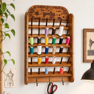 May include: A wooden thread rack filled with colorful spools of thread. The rack is adorned with a sewing machine design. A vintage Singer sewing machine sits on a wooden table, along with scissors, pins, and other sewing supplies.