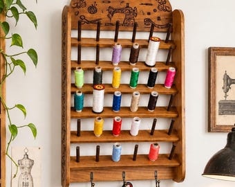 May include: A wooden thread rack filled with colorful spools of thread. The rack is adorned with a sewing machine design. A vintage Singer sewing machine sits on a wooden table, along with scissors, pins, and other sewing supplies.
