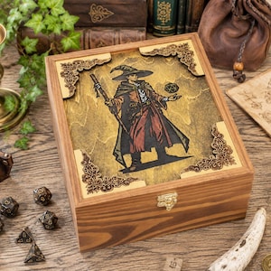 May include: A rectangular wooden box featuring a laser-engraved illustration of a wizard holding a staff and a twenty-sided die. The lid is adorned with ornate corner accents and a golden-brown finish, secured by a small metal latch on the front.