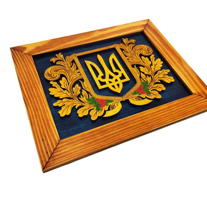 May include: A wooden framed wall art piece featuring a gold Ukrainian coat of arms with a blue background. The coat of arms is surrounded by gold floral designs.