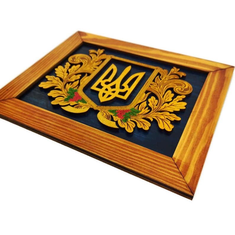 May include: A wooden framed wall art piece featuring a gold-colored Ukrainian trident emblem surrounded by intricate golden floral designs on a blue background.