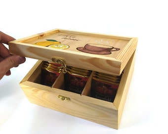 Könnte beinhalten: Holzkiste für Tee mit einem Scharnierdeckel. Der Deckel ist mit einem Zitronen- und einem Teebecher-Motiv verziert, aus dem Dampf aufsteigt. Die Box hat sechs Fächer für Teebeutel. Der Text auf dem Deckel lautet "Tea Time".