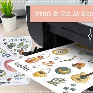 May include: A white sheet of paper with colorful stickers printed on it. The stickers feature camping and adventure themed illustrations, including a compass, a campfire, a guitar, and a mug of coffee. The paper is being fed into a printer with the text "Print & Cut At Home" on the front.