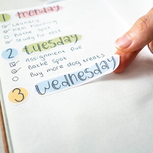 May include: A weekly planner with colorful stickers and handwritten to-do lists for Monday, Tuesday, and Wednesday. The list includes tasks like laundry, meal planning, and buying dog treats.