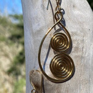 May include: A pair of gold-toned earrings with a teardrop shape and two spiral designs. The earrings are hanging from a wooden surface.