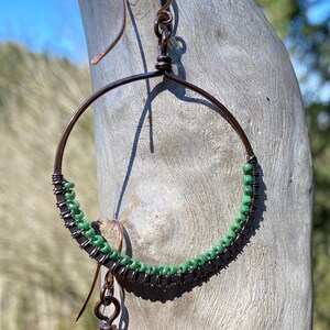 May include: A pair of copper hoop earrings with green beads. The hoops are a simple circle shape and the beads are evenly spaced around the hoop.