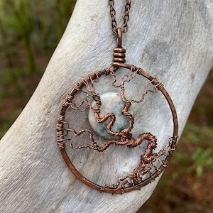 May include: A copper wire tree of life pendant necklace with a green and white agate stone. The necklace is on a copper chain with green and white beads.