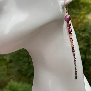 May include: A pair of long, dangling earrings with a copper chain and pink, brown, and clear beads.