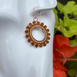 May include: Copper hoop earrings with a beaded design in shades of brown and gold.