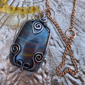 May include: A copper wire wrapped pendant featuring a multi-colored stone with a copper chain.