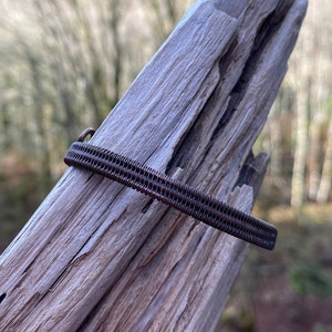 May include: A brown wire wrapped bracelet with a simple design. The bracelet is on a piece of weathered wood.