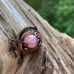 May include: A copper wire wrapped ring with a pink and white gemstone.