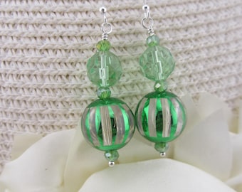 May include: A pair of green and silver beaded earrings. The earrings feature a silver hook, green beads, and two larger green and silver striped globe-shaped beads. The earrings are displayed on a white surface.