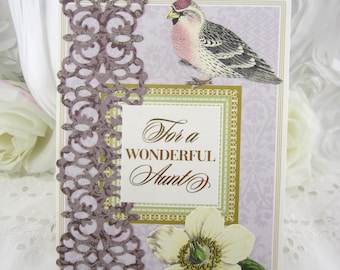 May include: A greeting card featuring a light purple background with a patterned design, a bird illustration, a white flower, and a brown die-cut lace border. The center text reads "For a WONDERFUL Aunt" in brown script and serif lettering.