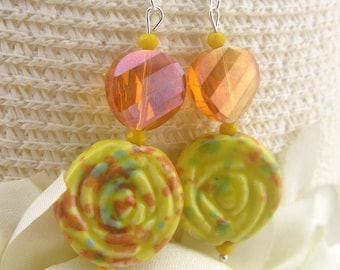 May include: A pair of dangle earrings featuring a combination of colors. The earrings have faceted orange and pink beads, yellow beads, and yellow rose-shaped beads with colorful speckles. The earrings hang from silver-colored hooks.