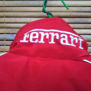 Puede incluir: Chaqueta roja con ribetes blancos y un logotipo "Ferrari" bordado en blanco en la parte posterior.