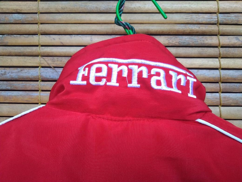 Puede incluir: Chaqueta roja con ribetes blancos y un logotipo "Ferrari" bordado en blanco en la parte posterior.