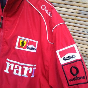 Puede incluir: Chaqueta roja Ferrari con ribetes blancos y logotipos bordados para Marlboro, Vodafone y Ovodafone. La chaqueta tambi&eacute;n tiene la palabra "Ferrari" bordada en la parte delantera.