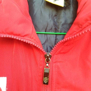 Puede incluir: Chaqueta roja con cremallera, con forro negro y un tirador de cremallera dorado con el logotipo de Ferrari. La chaqueta tiene una etiqueta amarilla con el logotipo de Ferrari en el interior del cuello.