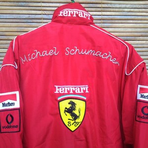Puede incluir: Chaqueta de carreras Ferrari roja con ribetes blancos, con el logotipo de Ferrari, las palabras "Ferrari" y "Michael Schumacher", y los logotipos de los patrocinadores Marlboro y Vodafone.