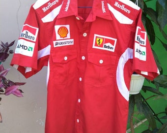 May include: Red short-sleeved button-up shirt with white accents and logos. The logos include "Marlboro", "Bridgestone", "Ferrari", and "AMD".