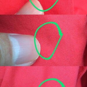K&ouml;nnte beinhalten: Nahaufnahme eines roten Stoffes mit einem kleinen dunklen Fleck, der in Gr&uuml;n eingekreist ist. Der Stoff hat eine gewebte Textur.