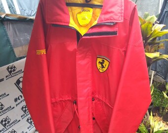 May include: A red Ferrari jacket with a yellow lining and a black zipper. The jacket has a large Ferrari logo on the front and the word "Ferrari" written on the left side of the chest.