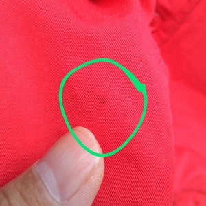 K&ouml;nnte beinhalten: Nahaufnahme eines roten Stoffes mit einem kleinen dunklen Fleck, der mit einem gr&uuml;nen Kreis umrandet ist.