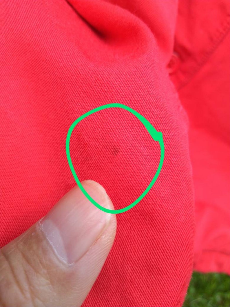 K&ouml;nnte beinhalten: Nahaufnahme eines roten Stoffes mit einem kleinen dunklen Fleck, der mit einem gr&uuml;nen Kreis umrandet ist.