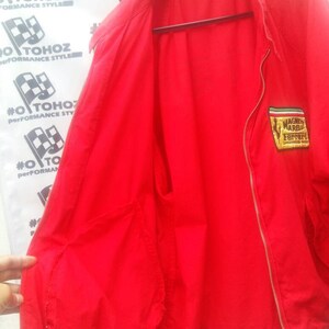 K&ouml;nnte beinhalten: Rote Windbreaker-Jacke mit Rei&szlig;verschluss und einem kleinen gestickten Aufn&auml;her auf der linken Brust, auf dem "Magni Marelli Ferrari" steht.
