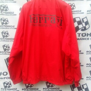 K&ouml;nnte beinhalten: Rote Windbreaker-Jacke mit einem schwarzen Ferrari-Logo und dem Text "Scuderia Ferrari" auf der R&uuml;ckseite.