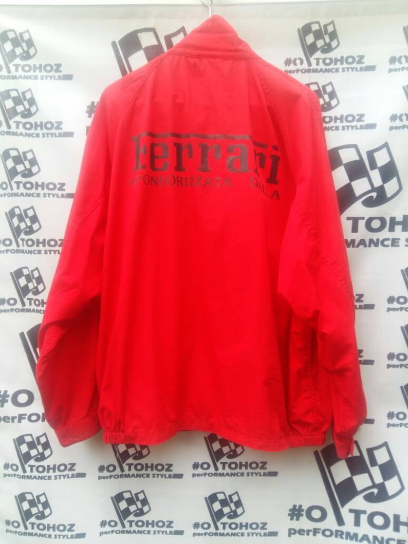 K&ouml;nnte beinhalten: Rote Windbreaker-Jacke mit einem schwarzen Ferrari-Logo und dem Text "Scuderia Ferrari" auf der R&uuml;ckseite.
