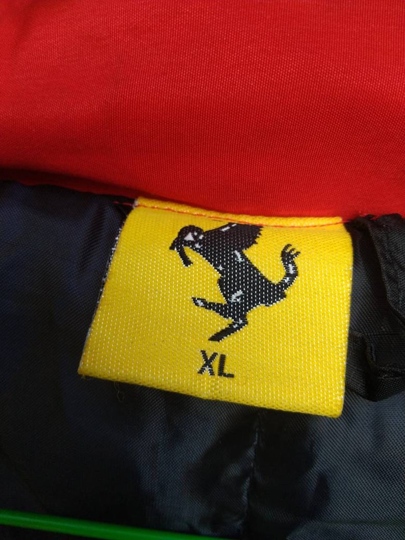 Puede incluir: Etiqueta de ropa amarilla y negra con un logotipo de caballo negro y el texto "XL".