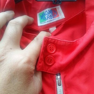 K&ouml;nnte beinhalten: Rote Jacke mit Rei&szlig;verschluss und zwei Kn&ouml;pfen. Die Jacke hat ein Etikett mit der Aufschrift "Magnerelli" und "Ferrari" auf dem Rei&szlig;verschluss.