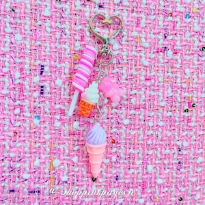 May include: A pink and white ice cream cone charm with a pink and white swirl ice cream cone, a pink and white swirl lollipop, and a pink and white ice cream sandwich charm attached to a silver key chain with a heart-shaped ring.