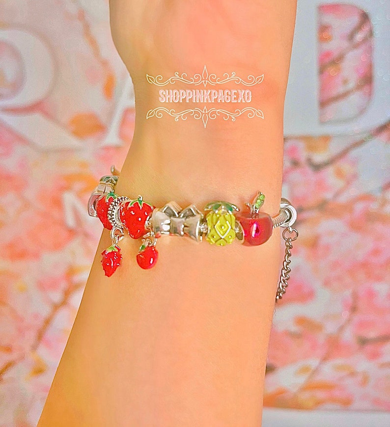 May include: A silver charm bracelet with a variety of fruit charms, including strawberries, apples, and pineapples. The charms are red, green, and yellow. The bracelet has a silver chain with a clasp.